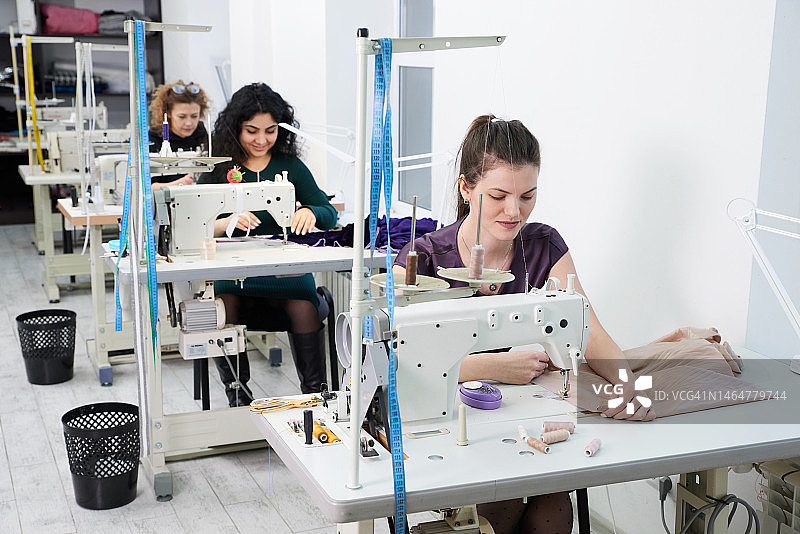 在裁缝工作室里用缝纫机缝制衣服的年轻女裁缝师们图片素材