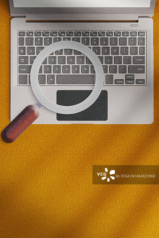 橙色背景上的笔记本电脑和放大镜图片素材