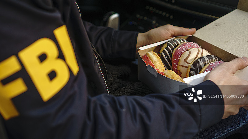 手里拿着一盒甜甜圈的联邦调查局探员图片素材
