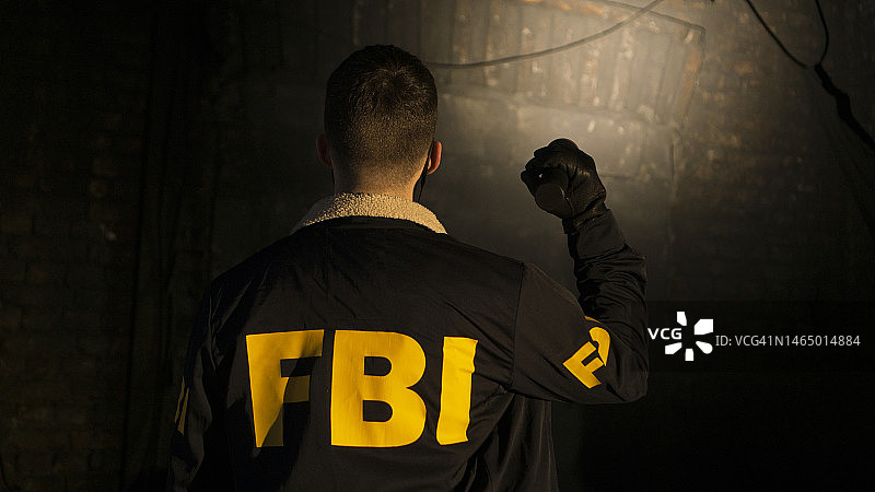 一名联邦调查局探员在黑暗的街道上用手电筒照着墙壁，身穿联邦调查局制服图片素材