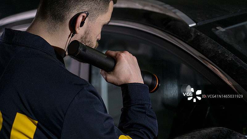 一位年轻的联邦调查局探员用手电筒检查黑暗车库里的一辆车图片素材