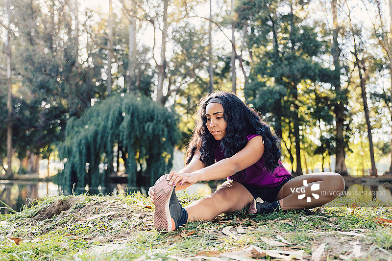 年轻本土马普切族越野跑者在森林训练前坐在地上伸展腓肠肌图片素材