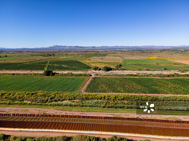 墨西哥奇瓦瓦州和美国得克萨斯州哈ancock堡之间的国际边境墙，阳光明媚的午后有果园和农田图片素材