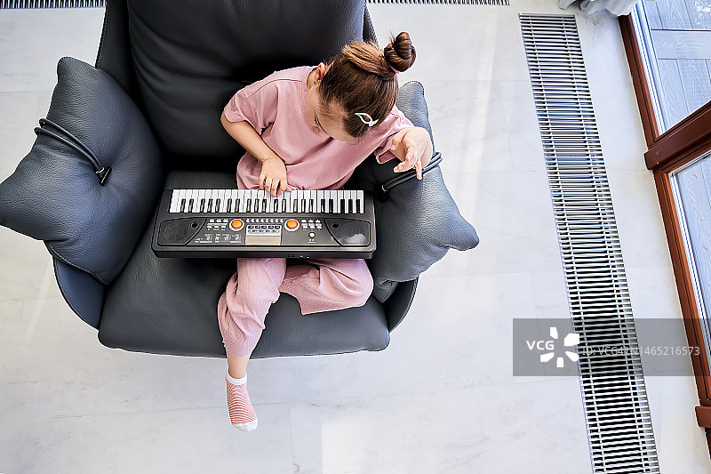 一位6岁女孩坐在窗边的扶手椅上弹奏电子琴图片素材