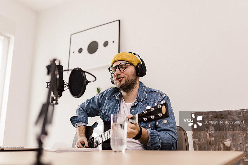 年轻微笑男子在录音棚使用麦克风和耳机录制播客并进行直播图片素材
