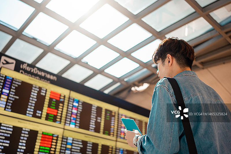 年轻男人在机场查看目的地列表，手持护照图片素材