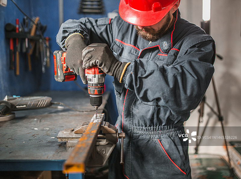 一名戴着红色防护头盔的产业工人在金属车间使用钻头图片素材