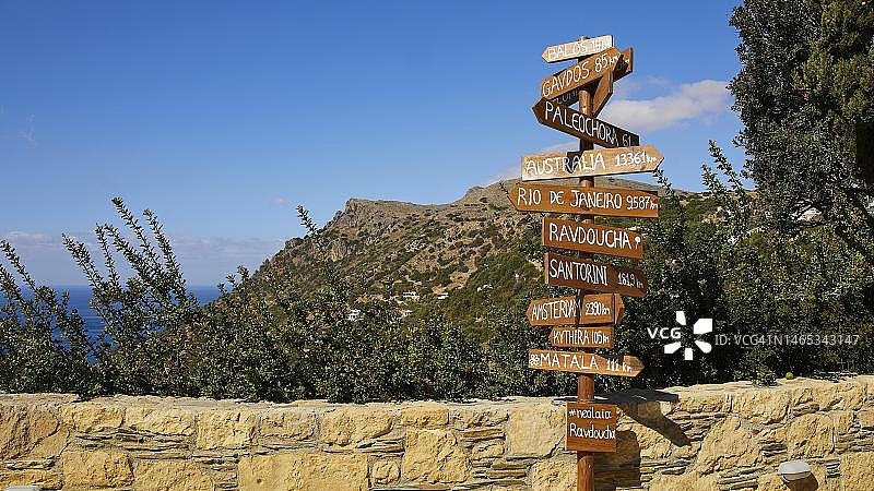 通往世界各地的木制路标，墙壁，蓝天白云，位于希腊克里特岛罗多波半岛西南部的拉夫杜查村图片素材