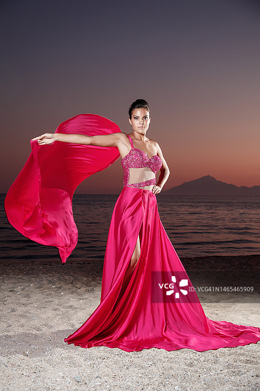 身穿红色上衣和面纱的年轻女子，穿着开衩长裙站在黄昏的沙滩上图片素材