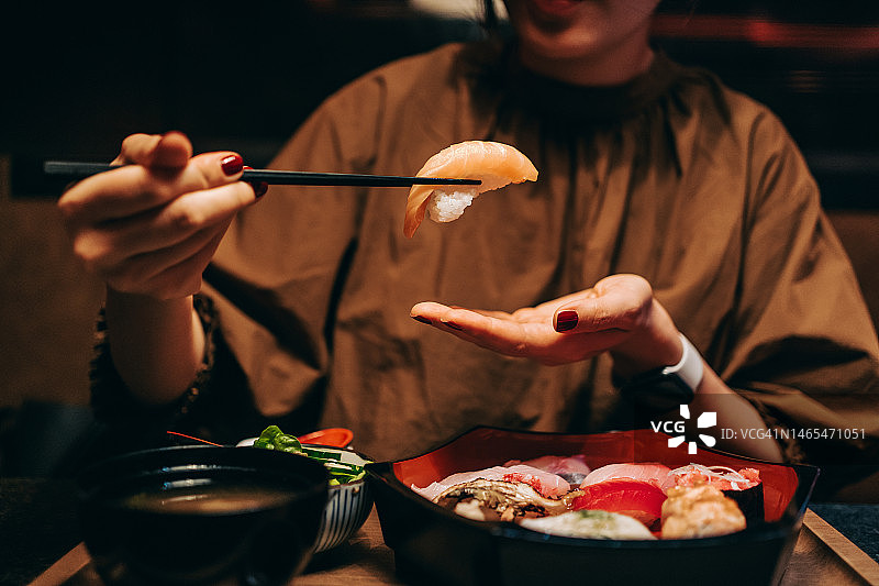 特写镜头：年轻亚裔女性在日式餐厅用筷子吃新鲜寿司，配味增汤和沙拉，亚洲美食概念图片素材