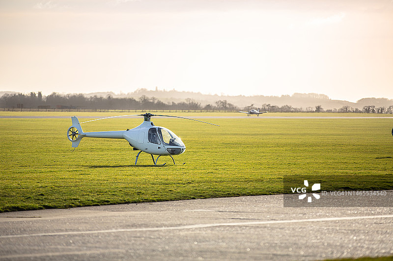 黄昏时停在机场草地上的小型直升机图片素材