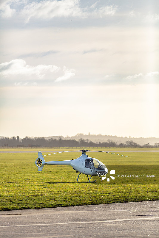 黄昏时停在机场草地上的小型直升机图片素材