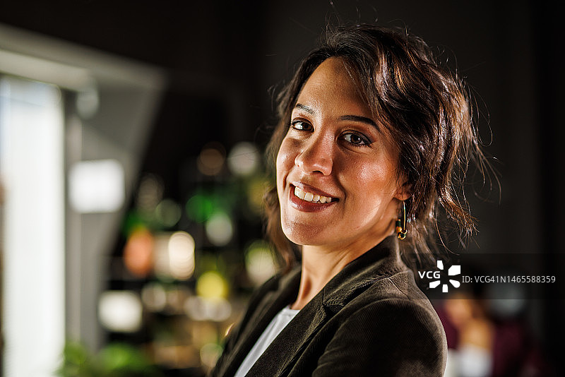 迷人的黑发女商人站在联合办公室内，对着镜头微笑图片素材