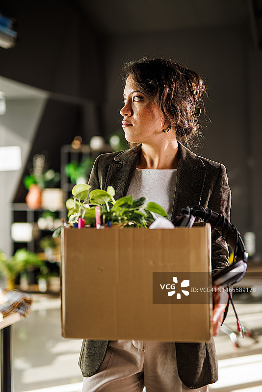 年轻女人在现代办公室拿着装有个人物品的盒子，被解雇后感到悲伤图片素材