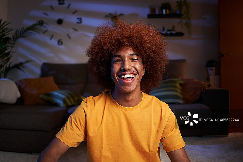 在家中看着镜头的年轻黑人男人，晚上坐在客厅里图片素材