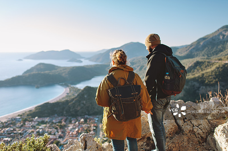 年轻情侣在日落时分的山中眺望大海图片素材