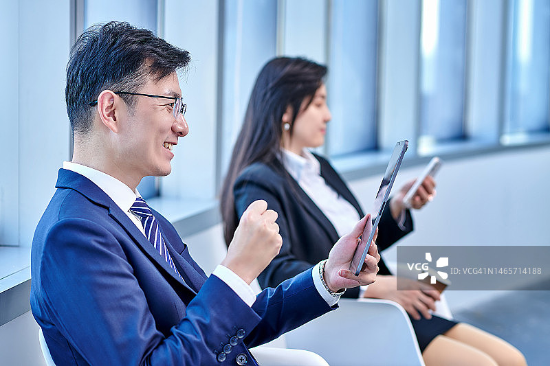 男同事兴奋地看平板电脑，女同事在远处就坐图片素材