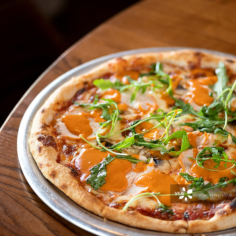 意式披萨：奶酪、火腿、酱汁和芝麻菜，传统烤箱烘焙。木桌金属盘，深色背景，柔焦图片素材