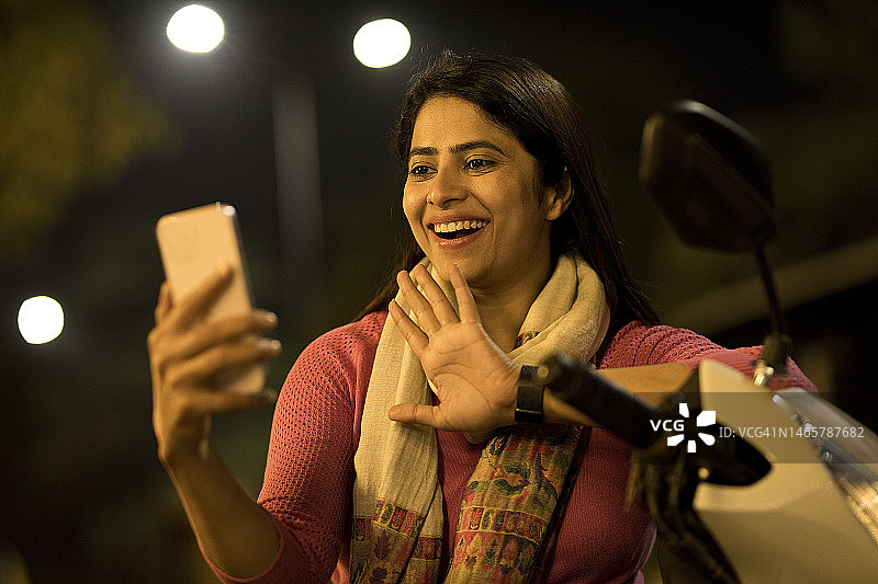 晚上在户外骑摩托车进行视频通话的快乐女人图片素材