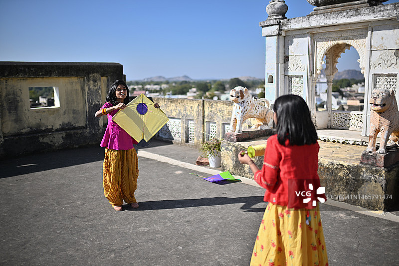 在阳台上放风筝庆祝Makar Sankranti节日的两个可爱女孩图片素材