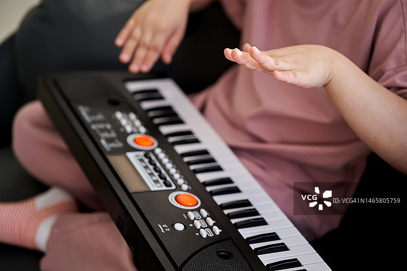 一位6岁女孩坐在窗边的扶手椅上弹奏电子琴图片素材