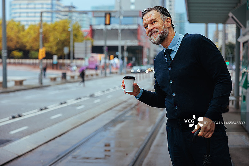 拿着咖啡等待交通工具的年长商人图片素材