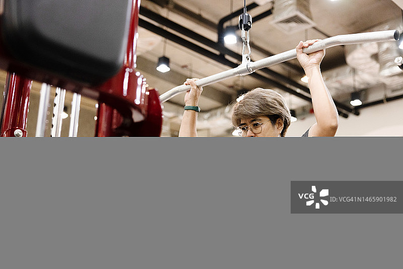 中年妇女在健身房使用背阔肌下拉训练器锻炼图片素材