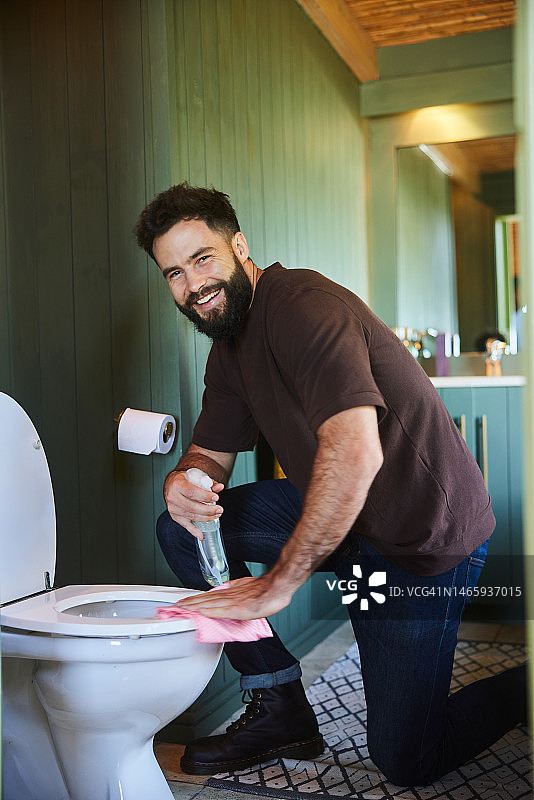 微笑的年轻男子用抹布和喷雾瓶清洁马桶图片素材
