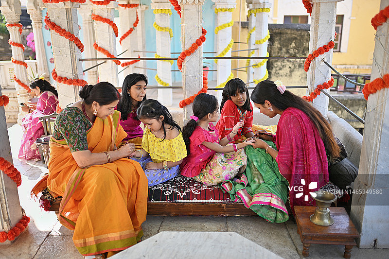家中祖母和姐姐为年幼女孩绘制印度海娜手绘图案，庆祝传统节日图片素材