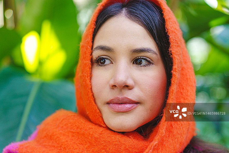 绿色自然背景上戴橙色围巾的委内瑞拉裔西班牙女性肖像图片素材
