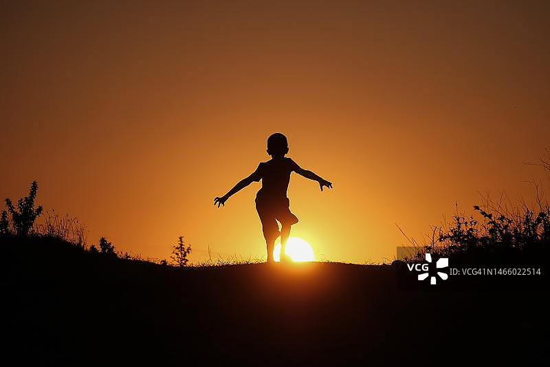 日落时分，奔跑在田野上的男孩的轮廓，印度尼西亚图片素材