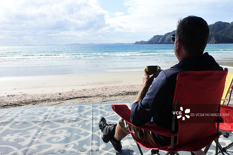 在新西兰海滩喝咖啡的年长男人背影图片素材