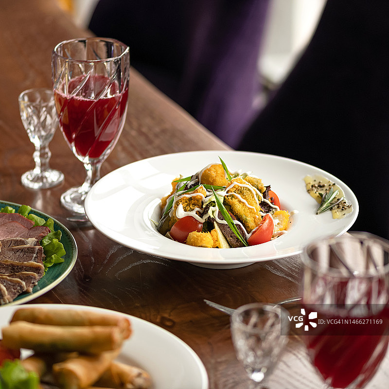 餐厅双人午餐：沙拉、冷盘、果汁饮品与餐具。木桌、紫色扶手椅，柔焦侧视图图片素材