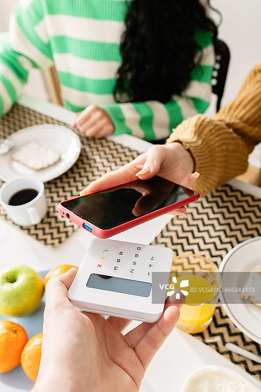竖版照片：年轻女人用手机App在无线终端上支付午餐图片素材