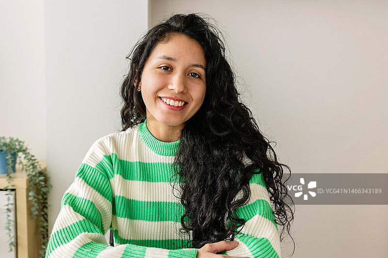 坐在桌旁对着镜头微笑的年轻拉丁美洲时尚女性肖像图片素材