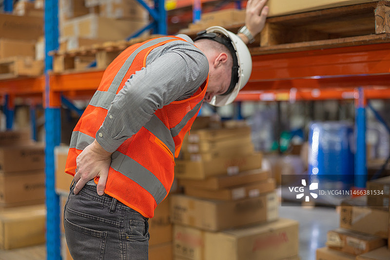一名男工人在仓库里抬箱子时背部受伤图片素材