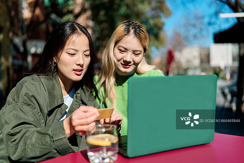 两个中国朋友在户外酒吧用信用卡和笔记本电脑购物图片素材