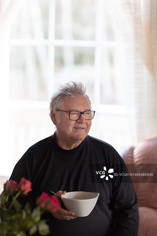 年长的男人喝汤并望向窗外，白天图片素材