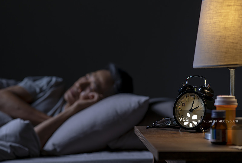 沮丧的亚洲老年男人躺在床上失眠图片素材