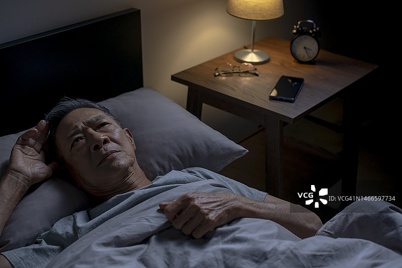 抑郁的亚洲老年男子躺在床上无法入睡，因为失眠图片素材