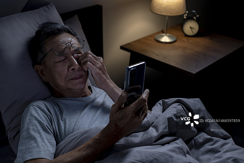 失眠老年亚洲男子在床上使用手机图片素材
