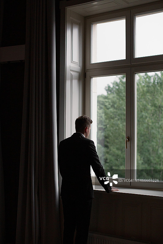 穿着深色西装透过窗户向外看的男人图片素材