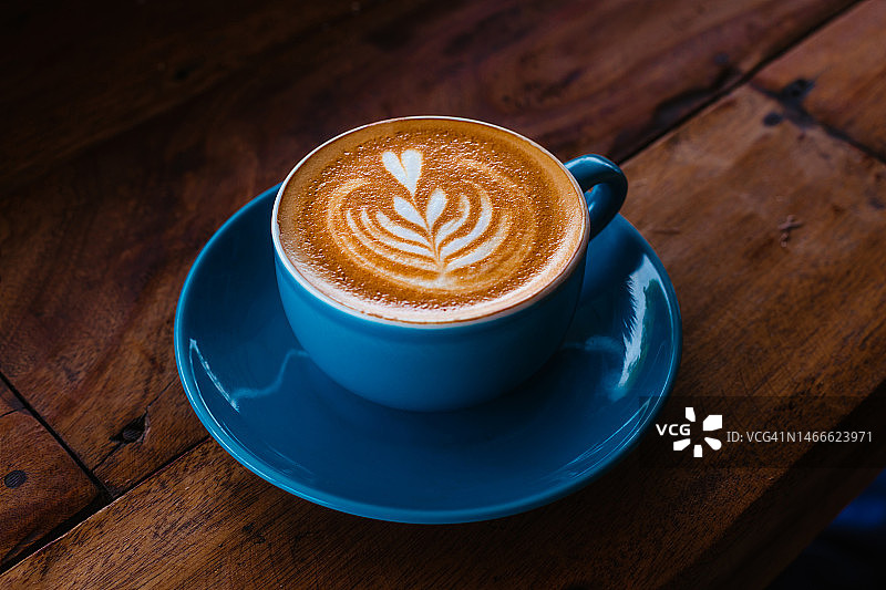 木桌上的蓝色陶瓷杯装卡布奇诺咖啡（侧视图）图片素材