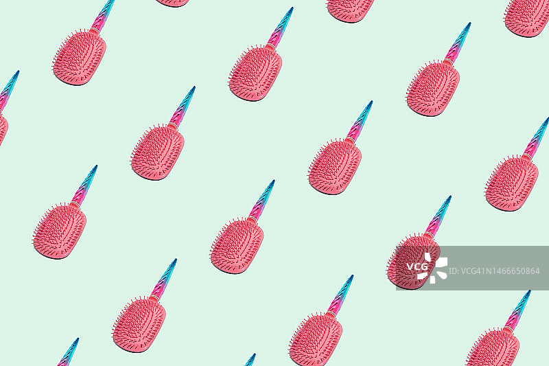 粉色按摩梳，手柄为彩虹色独角兽角造型，淡蓝色背景，护发概念图片素材