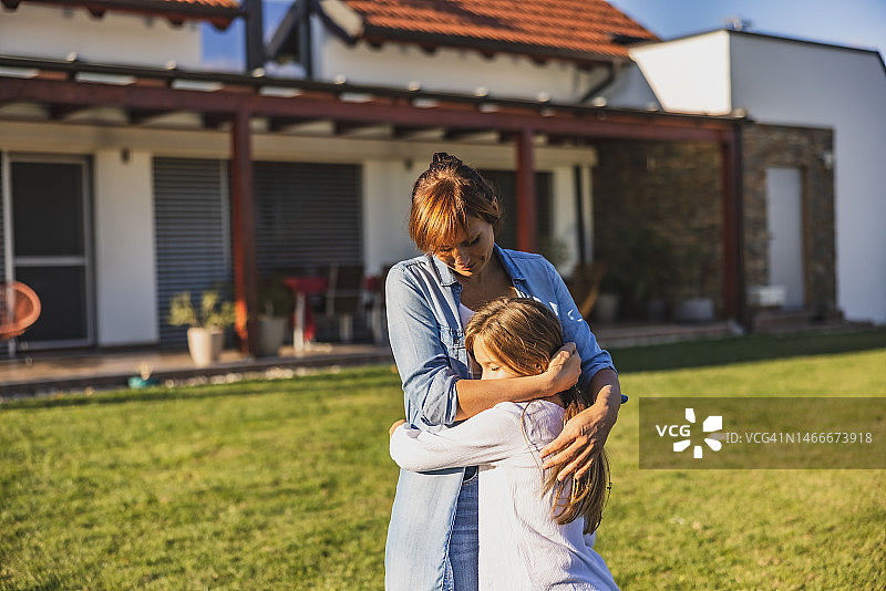 母亲在自家后院安慰小女儿，两人互相拥抱图片素材
