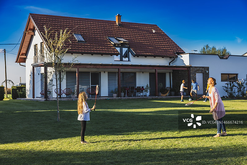 傍晚后院，母亲女儿打羽毛球，父亲儿子踢足球图片素材