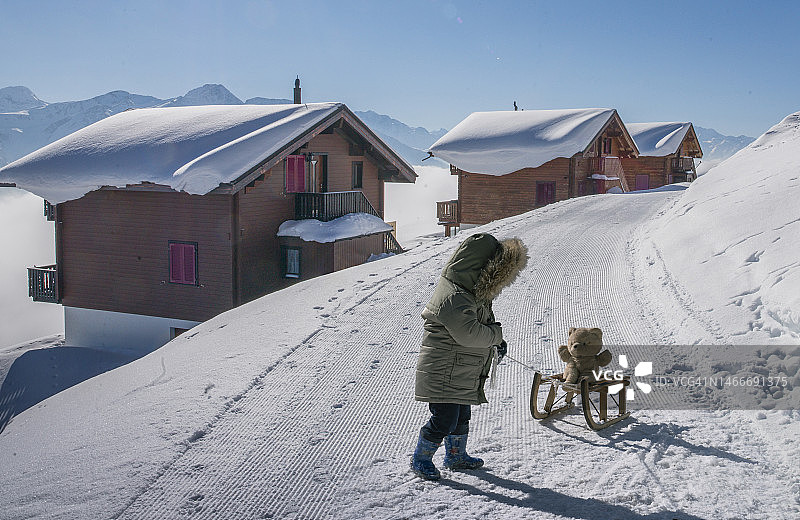 坐在雪橇上抱着泰迪熊的小男孩图片素材