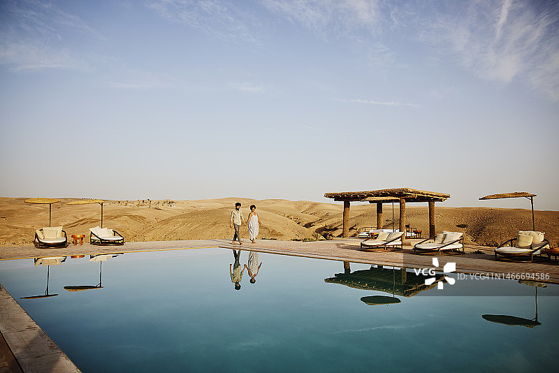 日出时分，情侣在沙漠营地的泳池边漫步图片素材