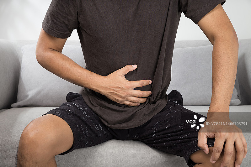 男子在泰国曼谷家中坐在沙发上肚子疼的中段视角图片素材