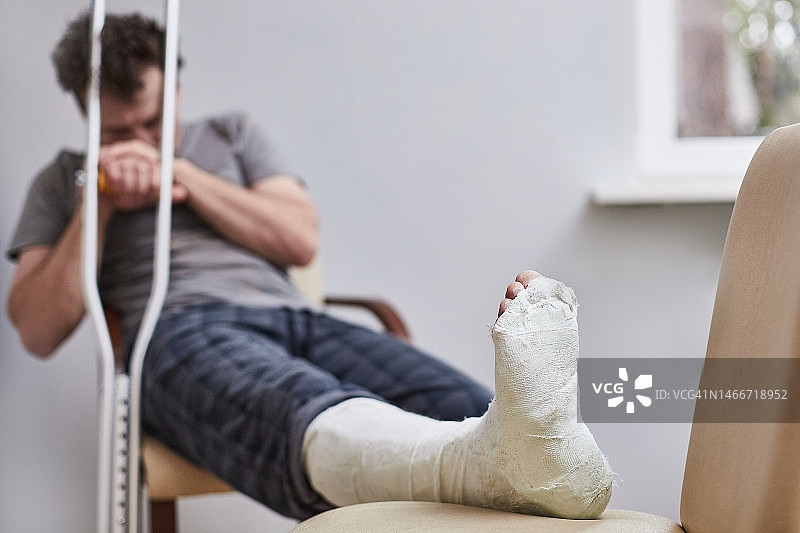 腿部受伤的悲伤男人坐在椅子上，疾病概念图片素材